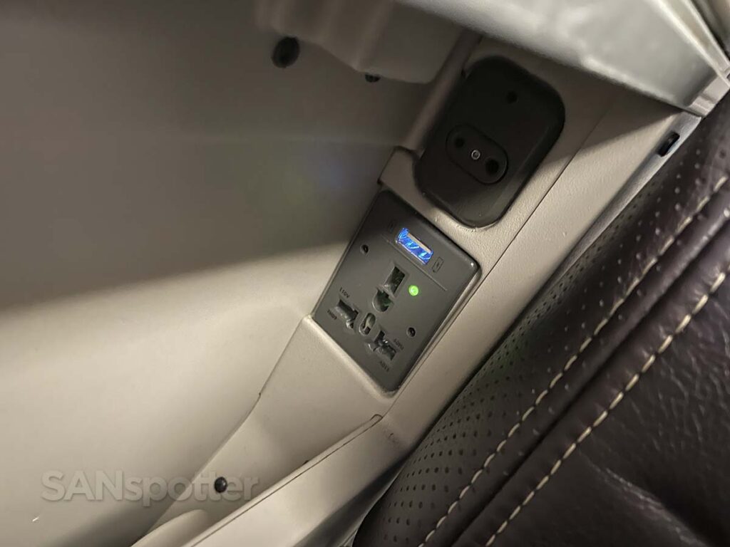 United Airlines 777-300ER Premium Plus 110 V power outlets and USB ports and audio jack located under the center armrest