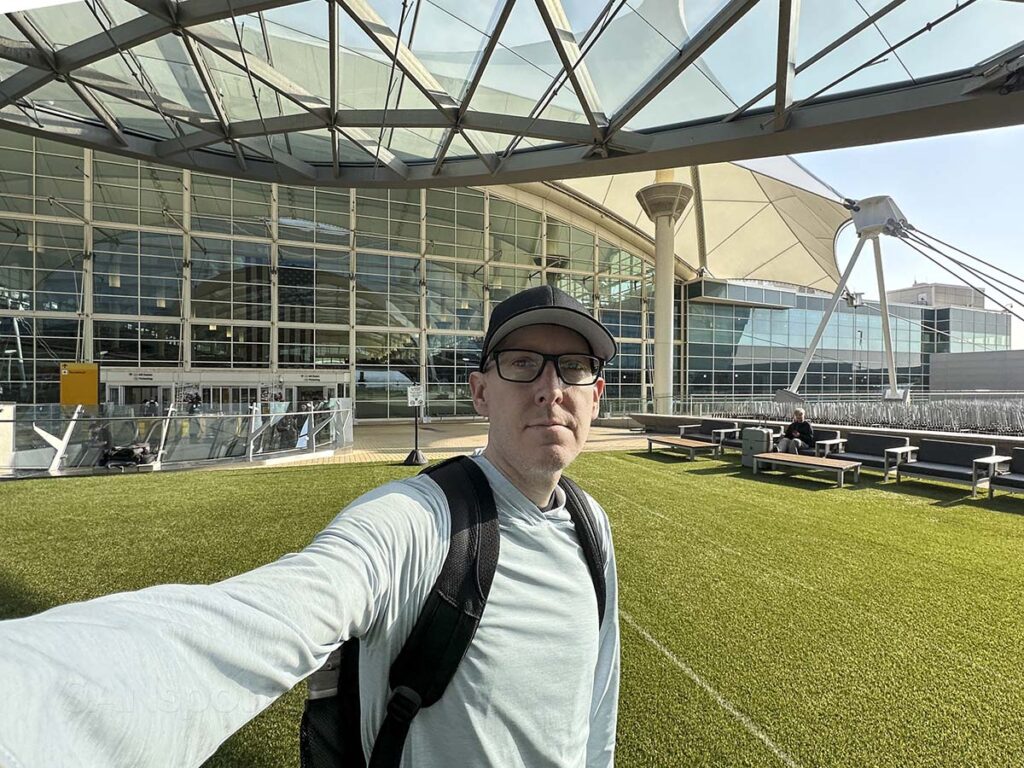 Scott Leazenby standing outside of the Denver International Airport in the grass covered plaza next to the Westin hotel