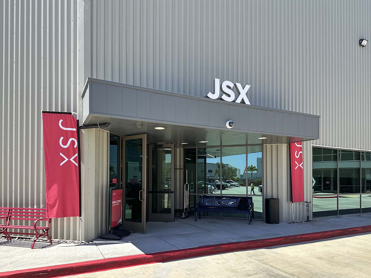 Main entrance to the JSX building at Carlsbad Jet Center at the McClellan-Palomar Airport featuring red and white JSX logos and banners